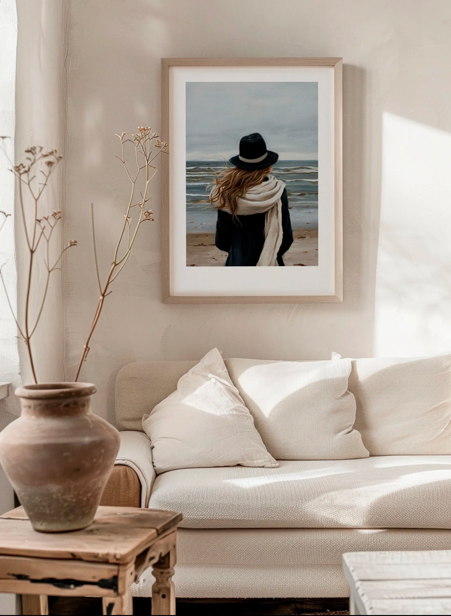 A Walk By The Sea poster in a modern Scandinavian living room with soft beige tones, neutral sofa and natural wood furniture, featuring calm blue, grey and sand coastal colors.