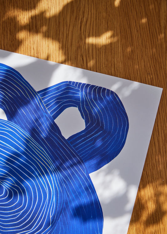 Detaljeret nærbillede af Shape No. 10 plakat med blå grafiske linjer på hvid baggrund, liggende på træbord med naturligt lys og skygger.