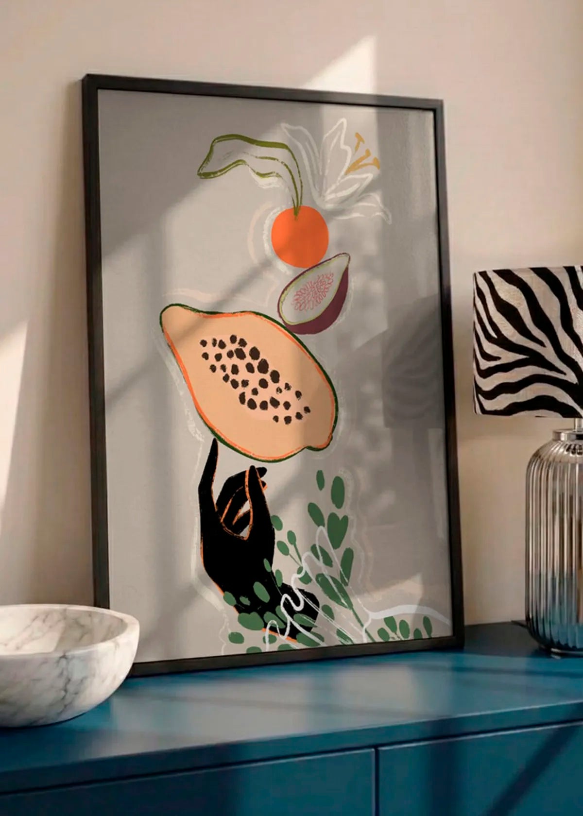 Indrammet frugtplakat med papaya og orange detaljer, stylet på en blå skænk i et varmt, moderne interiør.