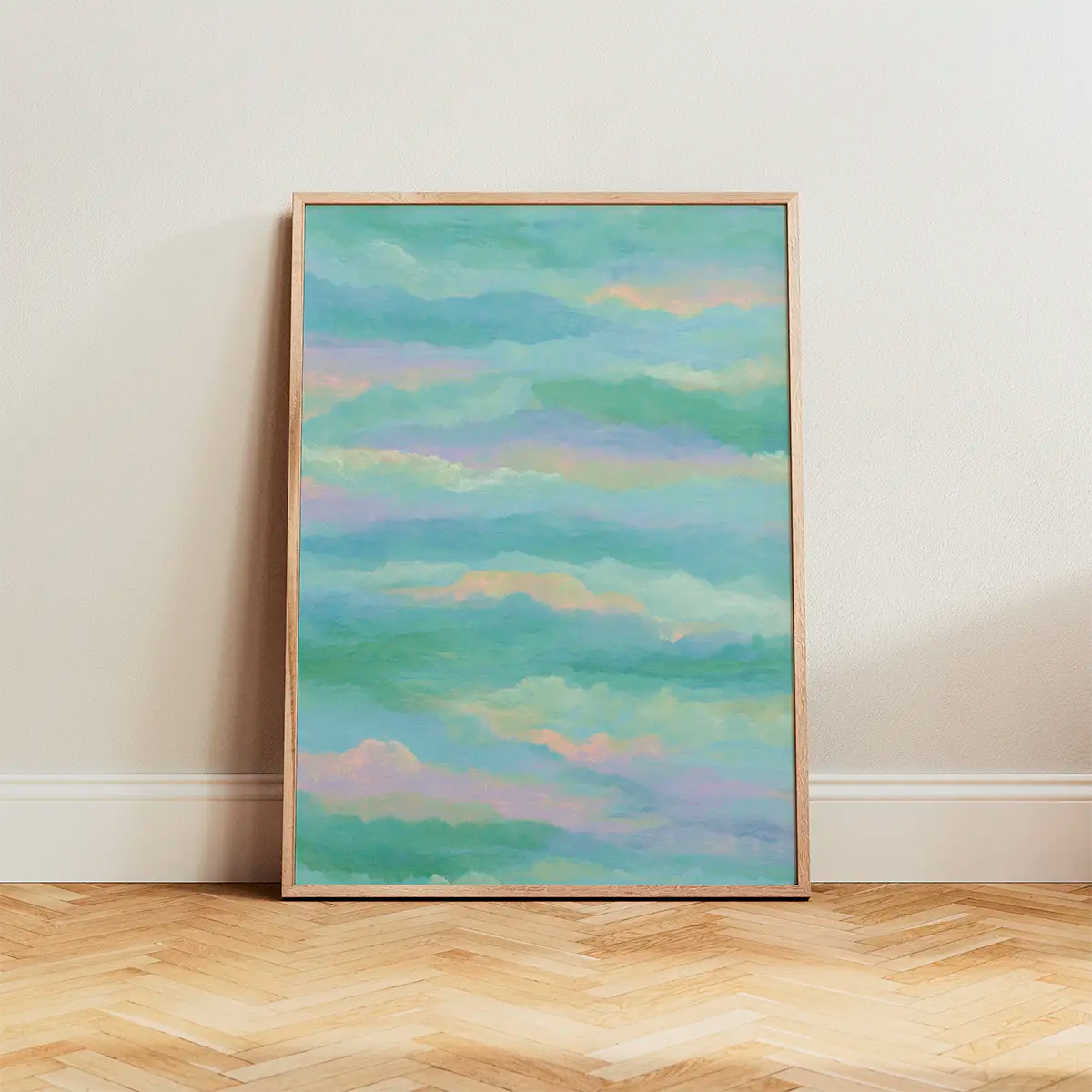 Pastel cloudscape poster in calm turquoise and pink hues, framed in oak and leaning against a white wall, styled on wooden flooring with soft daylight.