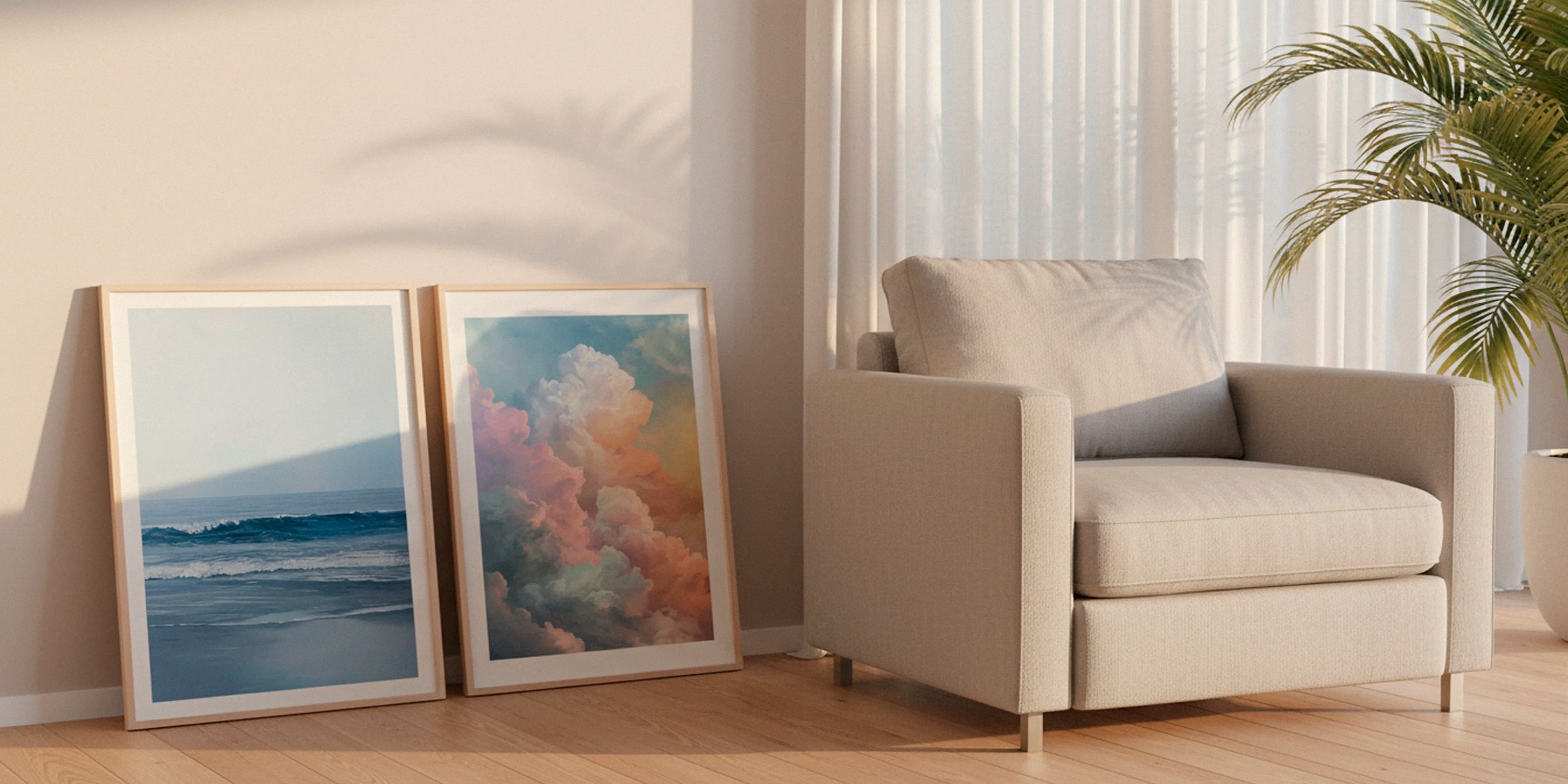 Two serene ocean and cloud posters in oak frames leaning against a wall beside a beige armchair, styled in soft Scandinavian daylight.