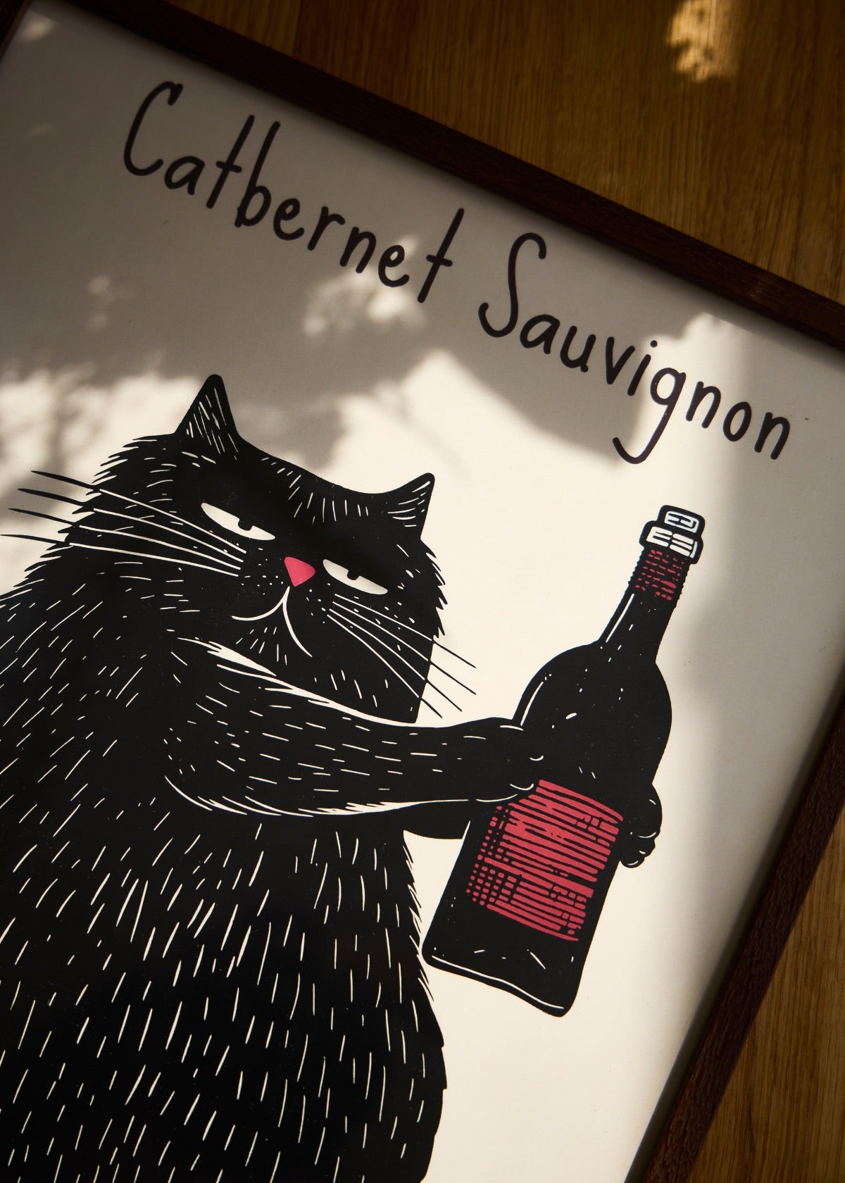 The Catbernet Sauvignon poster featuring a black cat and a wine bottle, shown in warm shadows on a wooden floor.
