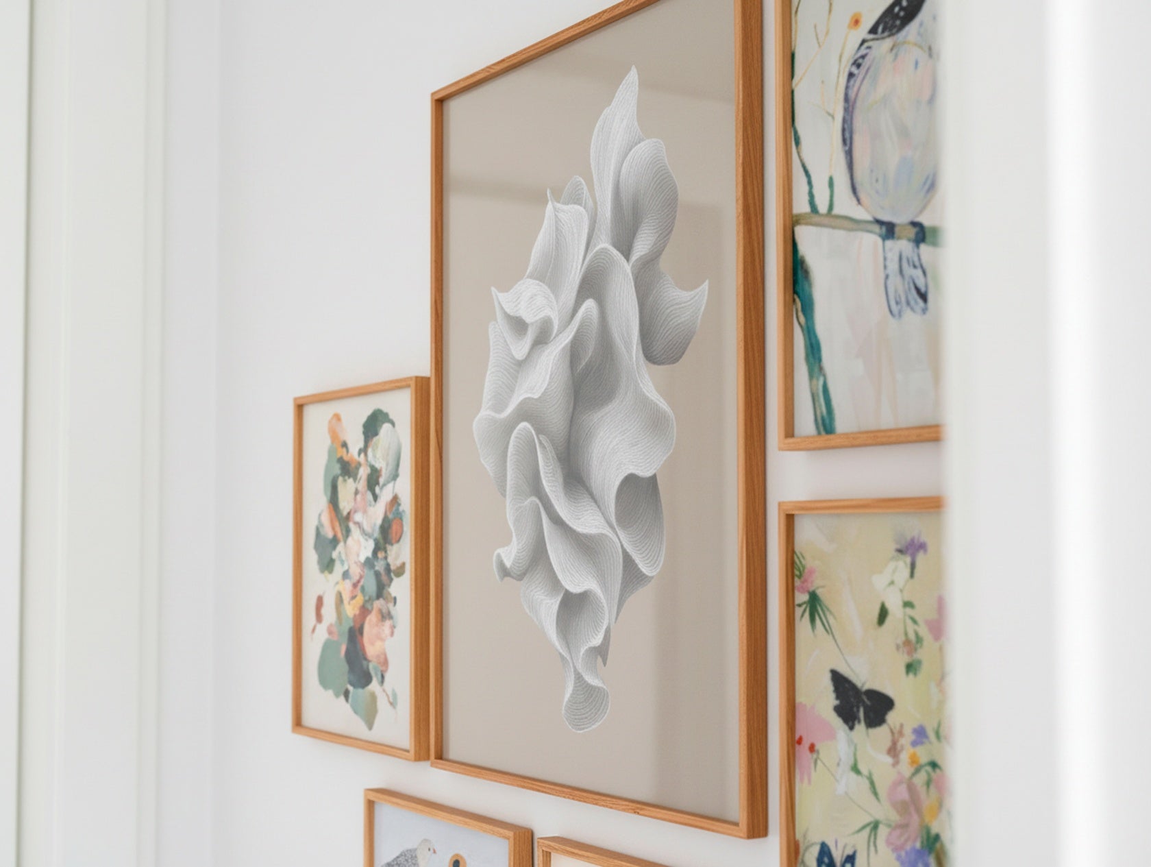 Close-up of a Scandinavian gallery wall showing a large white abstract poster beside botanical and bird-themed designs in oak frames.