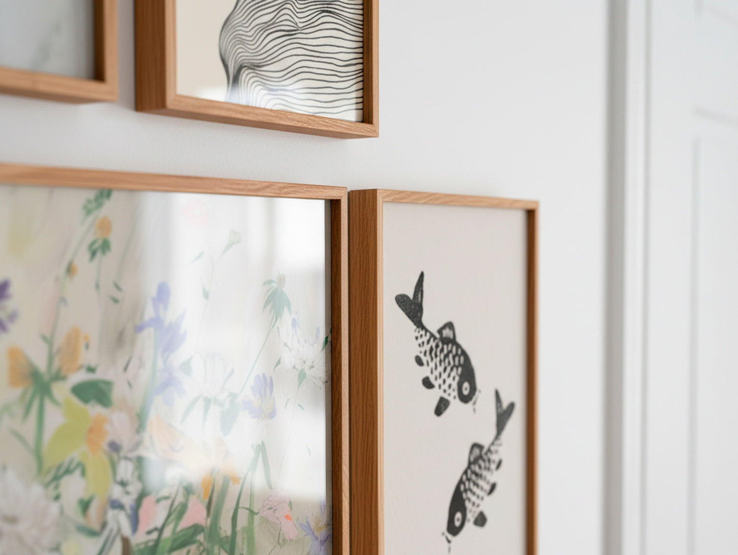 Close-up of oak frames featuring a floral poster and a black-and-white koi fish print on a light Scandinavian wall.