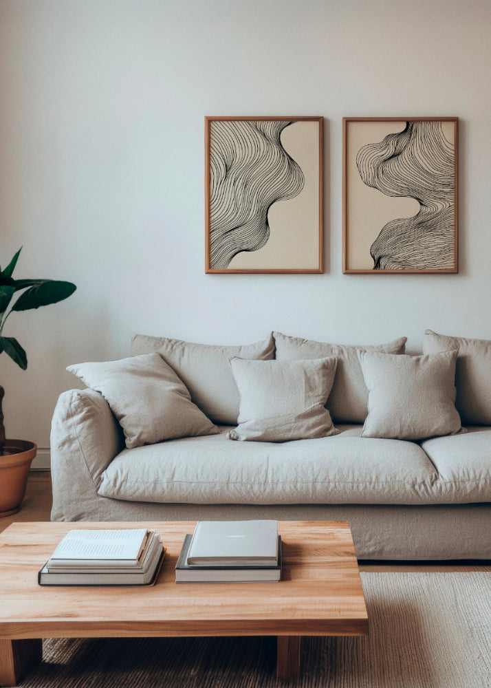 Miles and Tate posters featuring elegant black line art on a neutral beige background, framed in natural wood. The two artworks are displayed side by side above a cozy beige sofa, complemented by a wooden coffee table and a potted plant, creating a serene and minimalist living room ambiance.