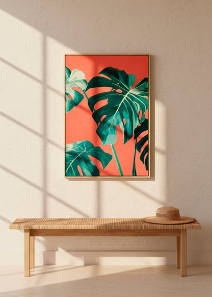 Framed “Monstera” canvas print with tropical leaves and bold coral tones, hanging above a woven bench in sunlit minimalist decor.