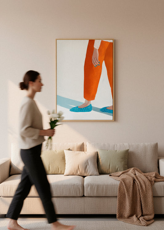 Framed “Moody Nails” canvas print above a beige sofa, with a blurred person walking by holding flowers in soft sunlight.