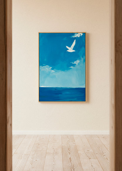 “Ocean” canvas print featuring a white bird flying above a deep blue sea under a clear sky, displayed in a bright minimalist room with wooden floors.