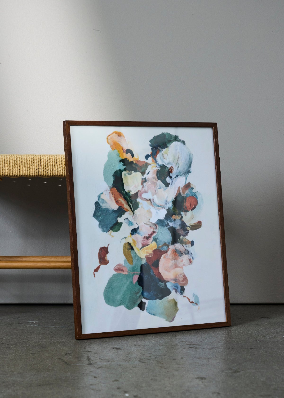 Petale poster from HelloPoster in dark wooden frame, featuring colorful abstract floral-inspired artwork, styled against grey wall with woven chair.