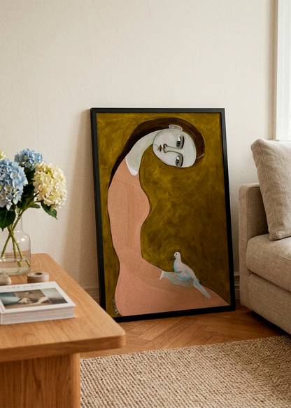 Serene Woman and Dove by Sharyn Bursic displayed in a black frame, leaning against a soft cream wall beside a beige sofa and wooden coffee table in a warm, elegant living room.