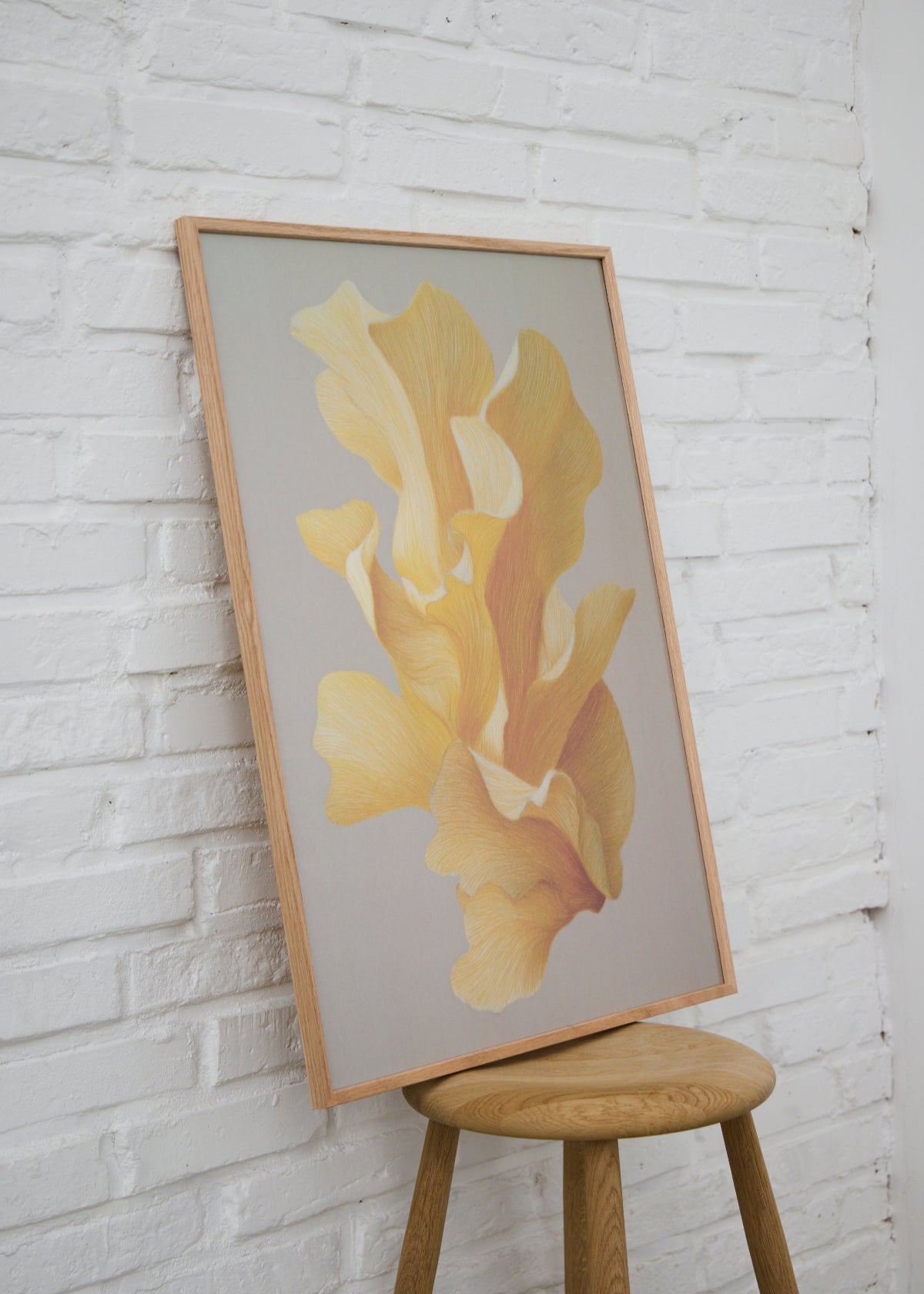 Shape no. 60 poster from HelloPoster in oak frame leaning against white brick wall, with abstract yellow design on grey background