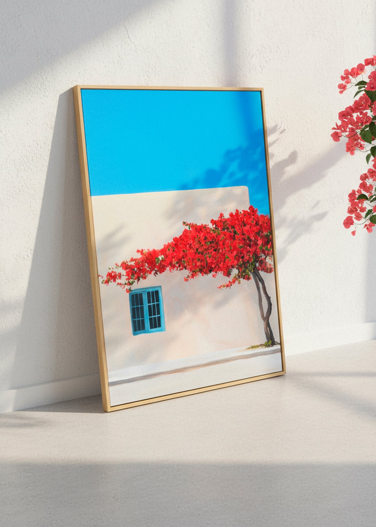 “Siesta” canvas print featuring a bright Mediterranean house with red flowers against a vivid blue sky. Displayed in a modern beige room with sunlight and soft shadows.