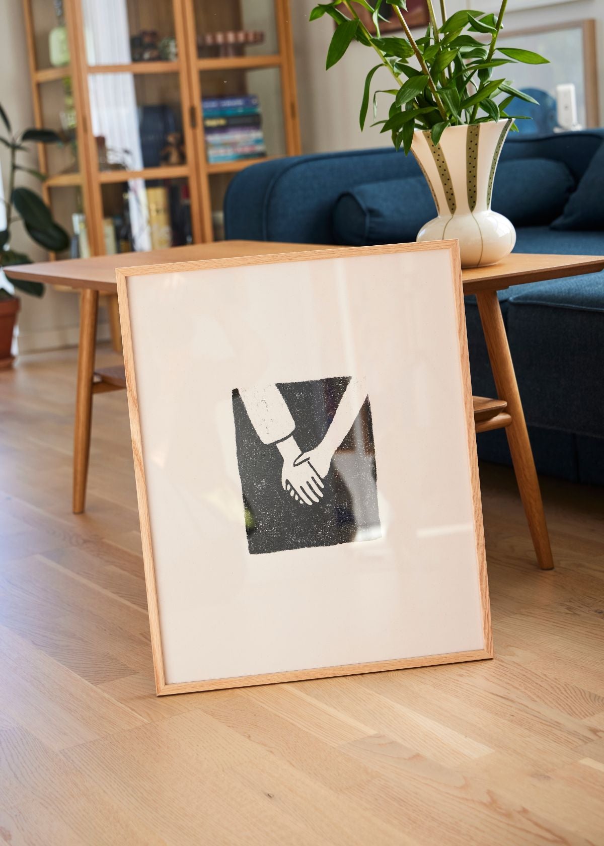 Togetherness poster in light wooden frame styled on a shelf with colorful mugs and Scandinavian ceramics.