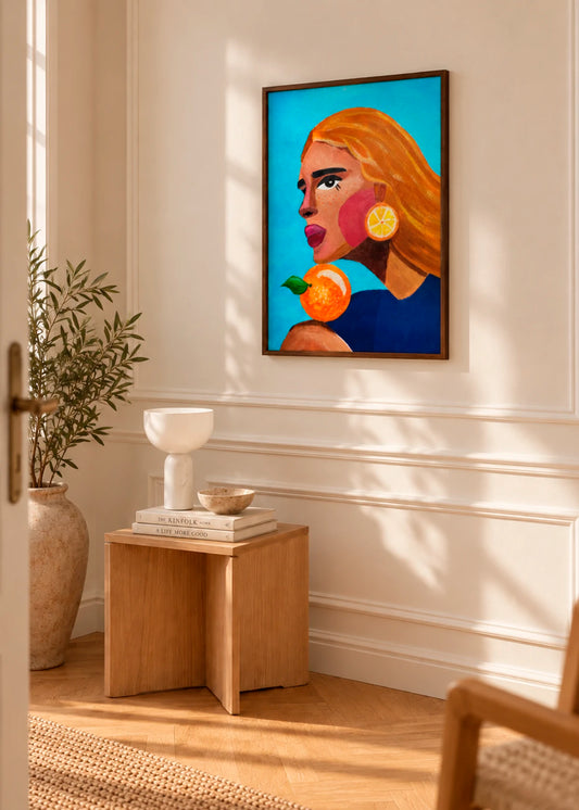 Woman With Orange plakat af Raissa Oltmanns i mørk træramme, stylet på en lys væg i et varmt nordisk interiør med træ og naturligt lys.