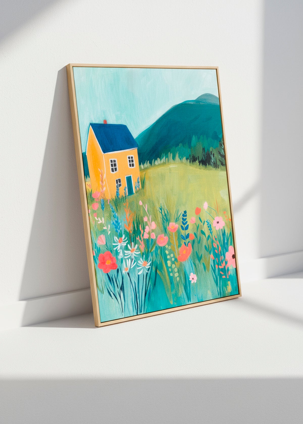 Framed Yellow House canvas leaning against a white wall in soft sunlight, showing a meadow full of colorful flowers.
